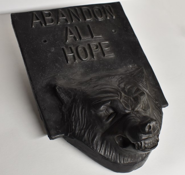 A cast iron artwork with "Abandon All Hope" written above a wolf's head