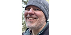 Close-up of a smiling man in a gray fleece beanie.