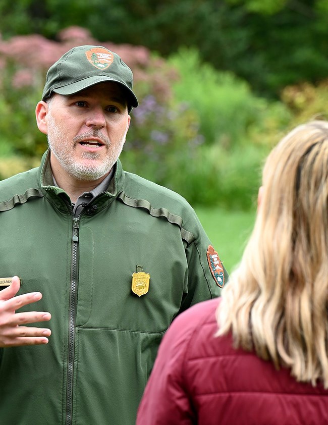 Man in NPS uniform faces the camera as he talks to a woman.