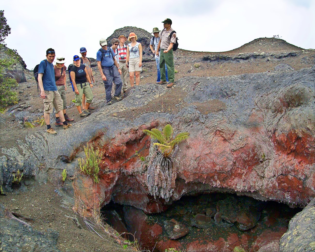 Ranger talk in Hawai'i Volcanoes National Park Service ranger talking and gesturing to a group of visitors about a fissure in the lava rock beneath them.