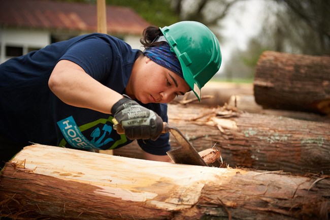 A member of the HOPE Crew shaves down a timber. A member of the HOPE Crew shaves down a timber.