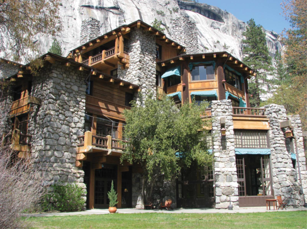 A large stone building with wooden trim sits in front of a stone mountain with trees