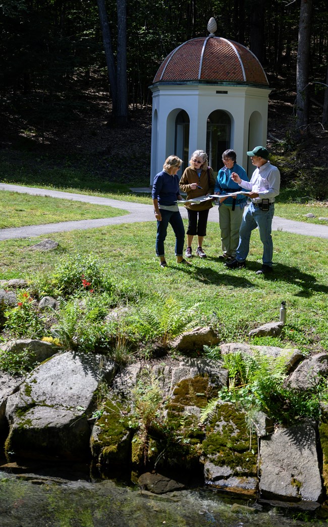 An artist speaks with three visitors with a domed spring house in the background An artist speaks with three visitors with a domed spring house in the background