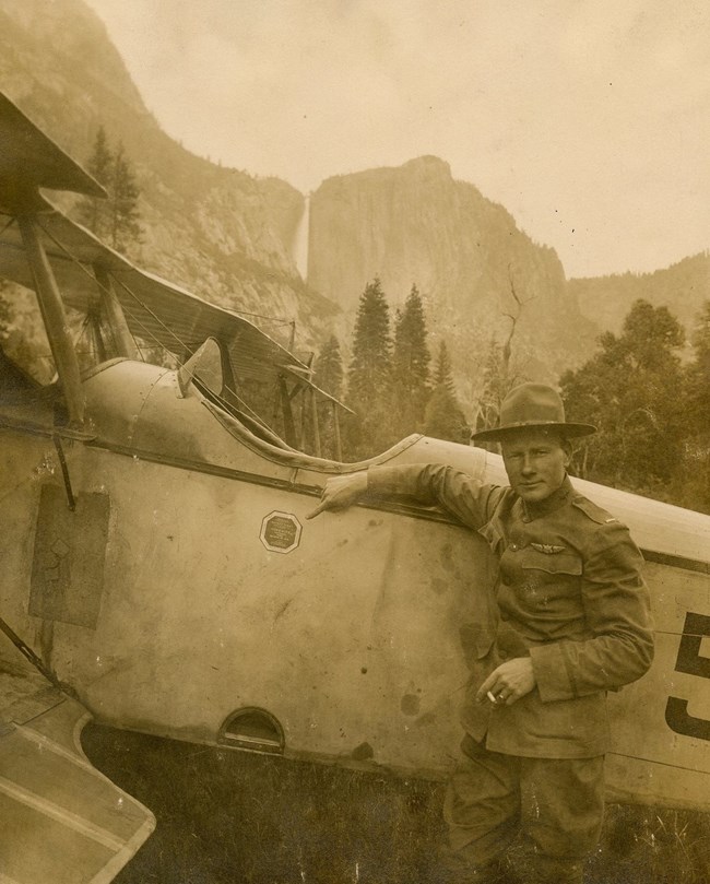 Man stands next to a bi-wing plane pointing at a sticker on its side.