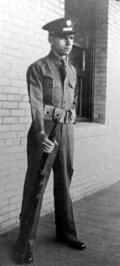 A man in uniform stands holding a rifle