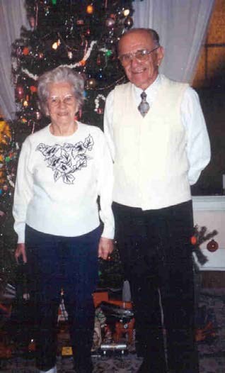 an elderly white couple stand in front of a Christmas tree