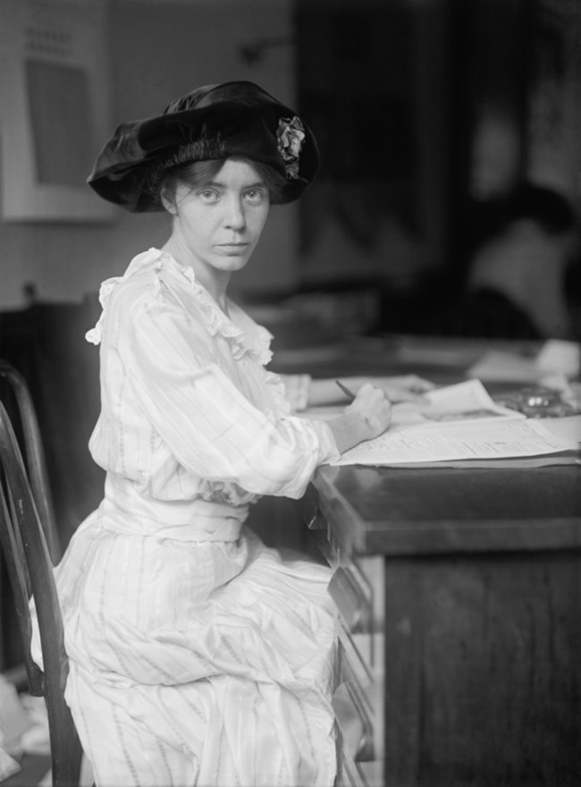 black and white portrait of Alice Paul seated at a desk. LOC