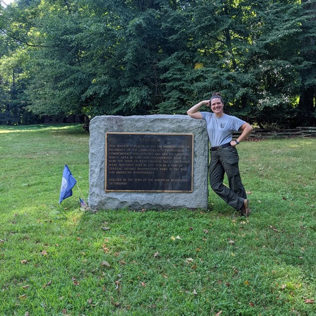 A uniformed park employee leans against a cement monument