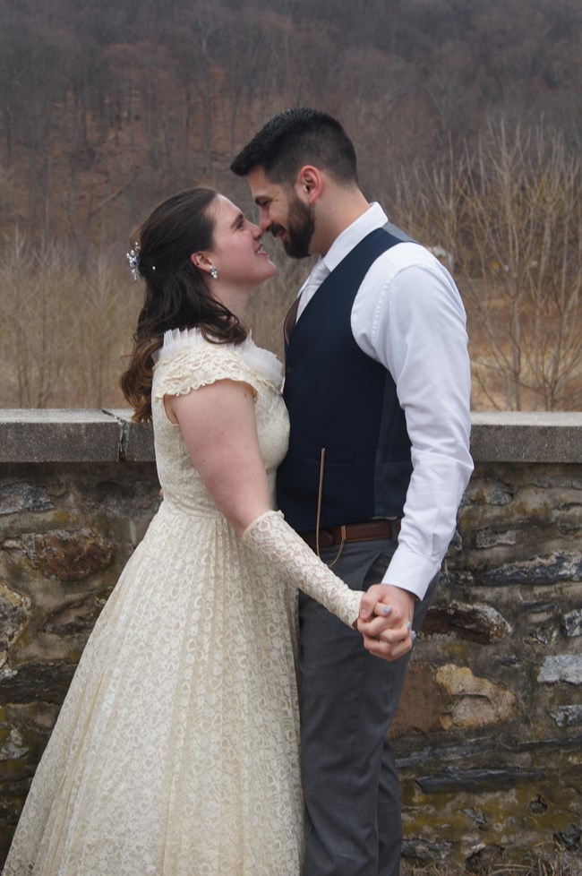 A bride and groom smile and hold hands outside.