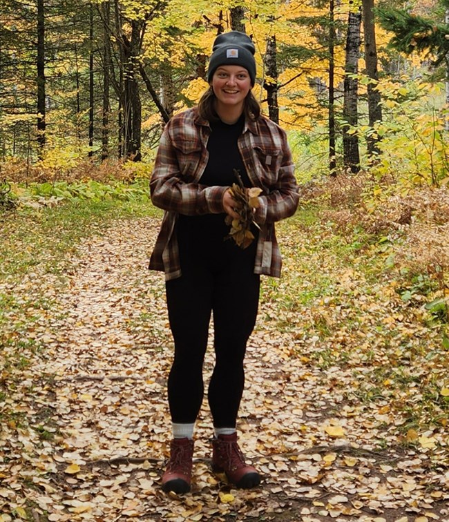 Alyssa Sanderson Woman standing on a path in the woods surrounded by fall colors