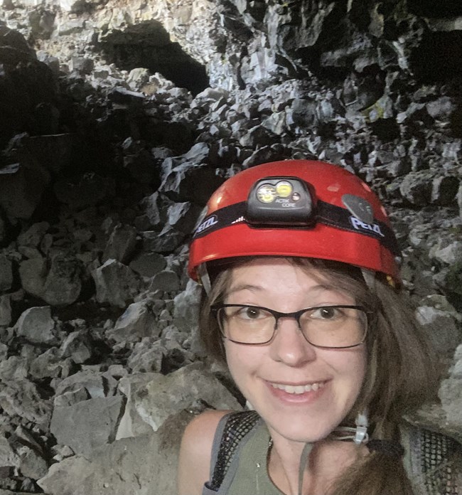 Smiling face of young woman with helmet and headlamp in a cave .