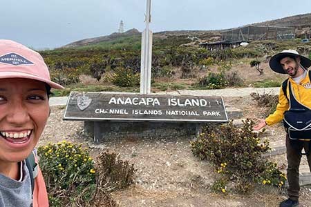 Woman excitedly smiles in selfie of her and hiking partners standing at Channel Island welcome sign