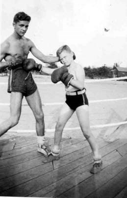 a young man stands next to a child, both wearing shorts and boxing gloves