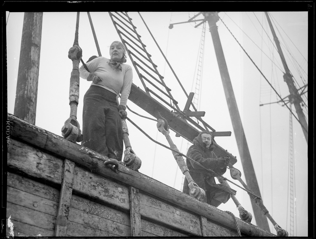 AnnSherwinandWilliam-LeslieJones-BPL looking up at a young man and woman standing on the edge of a ship holding on to ropes.