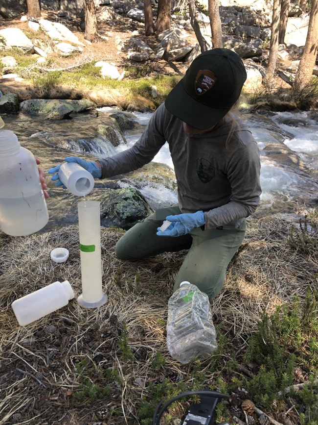 Preparing for a salt dilution discharge measurement at a river in Yosemite National Park Scientist kneels at the edge of a river and pours liquid into a graduated cylinder, preparing for a salt dilution hydrology measurement.