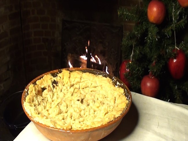 A crumble/pie style food sitting in a dish next to a christmas tree covered in apples.