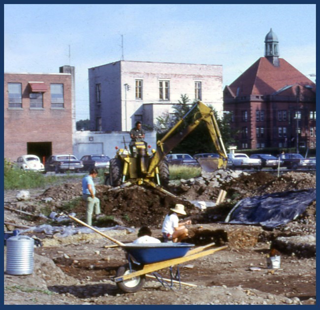 Archaeological excavations at Fort Stanwix. Lots of earth is moved around and dug open. A few people examine the area.