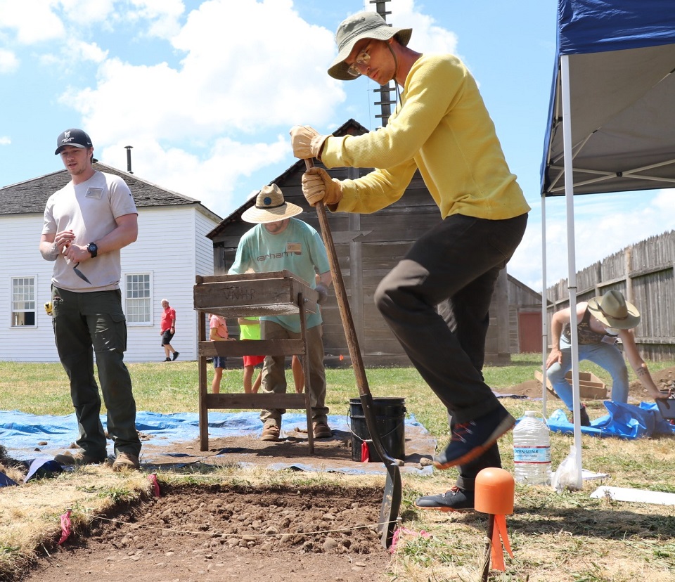 On a sunny day, students use shovels to break ground at an archaeological site inside Fort Vancouver.