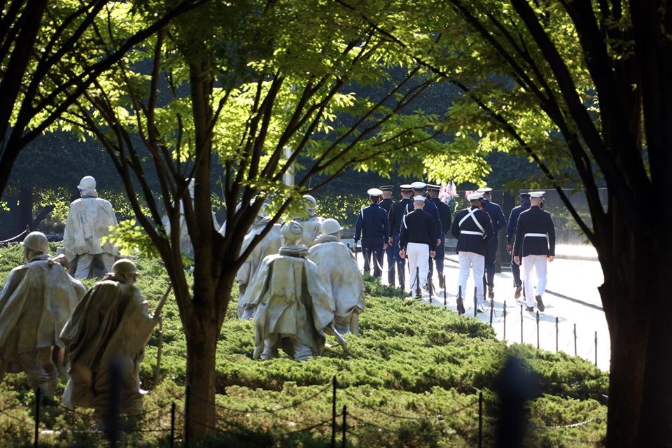 Men in uniform walk next to the wall at the Korean War Veterans Memorial.