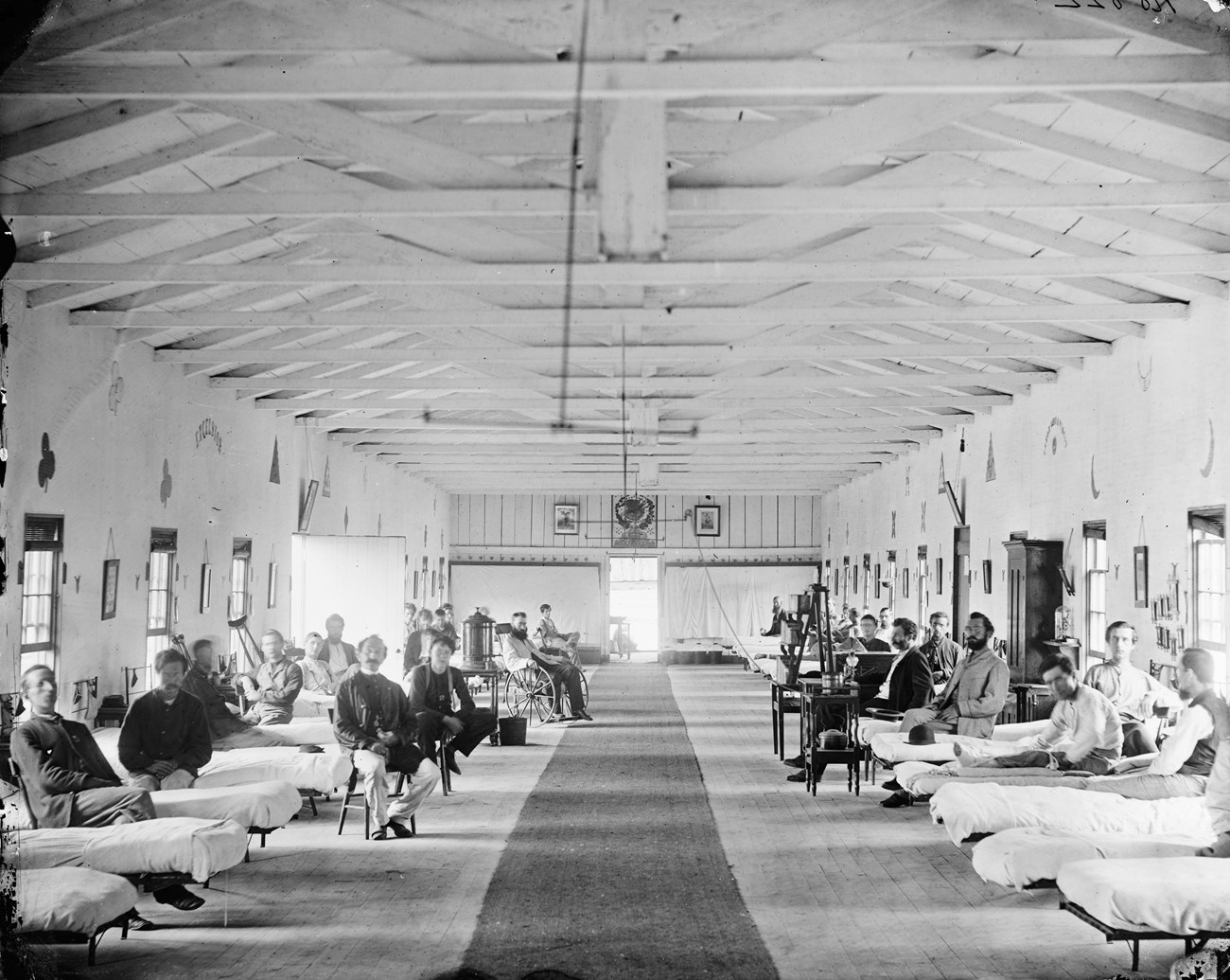 A long, open hospital wing with two lines of beds and soldiers sitting up, looking at the camera.