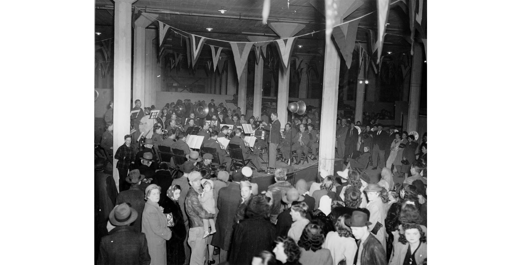 Photo 4: Army Air Force Band Forum Black and white photo of a large room decorated with penants and packed with people. In the background is a band on a low stage.