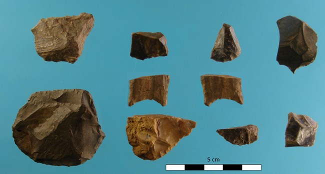 Ten stone tool artifacts displayed on a blue background with a 5 cm ruler. Artifact size ranges from 2.5 cm to 5 cm