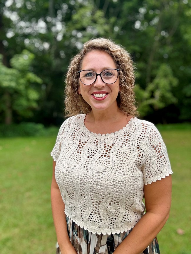 Ashley Baggett A woman with curly hair and glasses smiles for the camera.