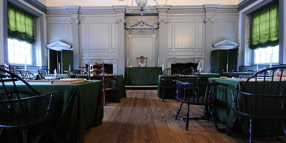Interior view of a meeting room with two rows of tables facing a central table on a raised platform.