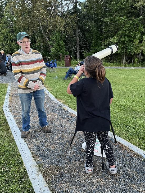 Photograph of a child looking through a telescope while an adult stands nearby.