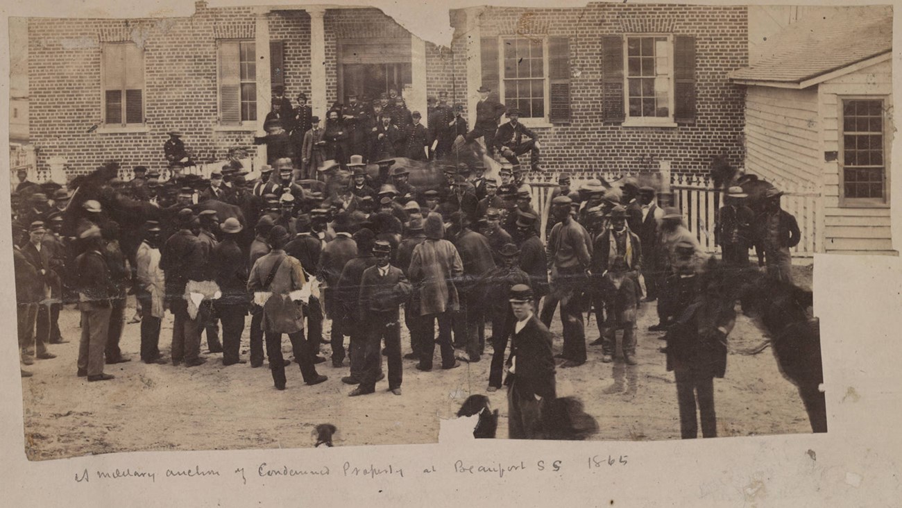 Tax Auction Beaufort 1865 A large group of men stand in front of a building looking at an auctioneer.