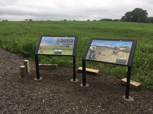 Two side by side wayside exhibits sit in front of a grassy prairie.