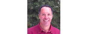 Smiling man in red shirt stands in front of green leafy vegetation