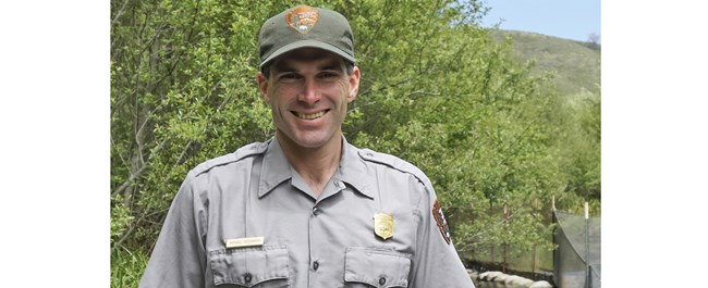 Reichmuth in a National Park Service cap and uniform, smiling outside by creek.