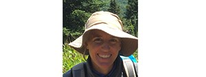 Smiling woman in a white hat on a sunny day. Green vegetation is in the background