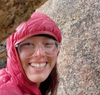Avery Sigarroa Woman standing near rock wearing a hooded down coat and smiling.