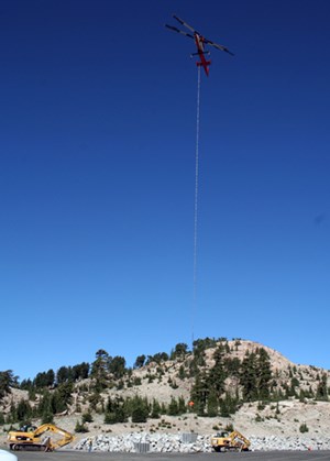 A helicopter with a suspended load hovers over a dry landscape