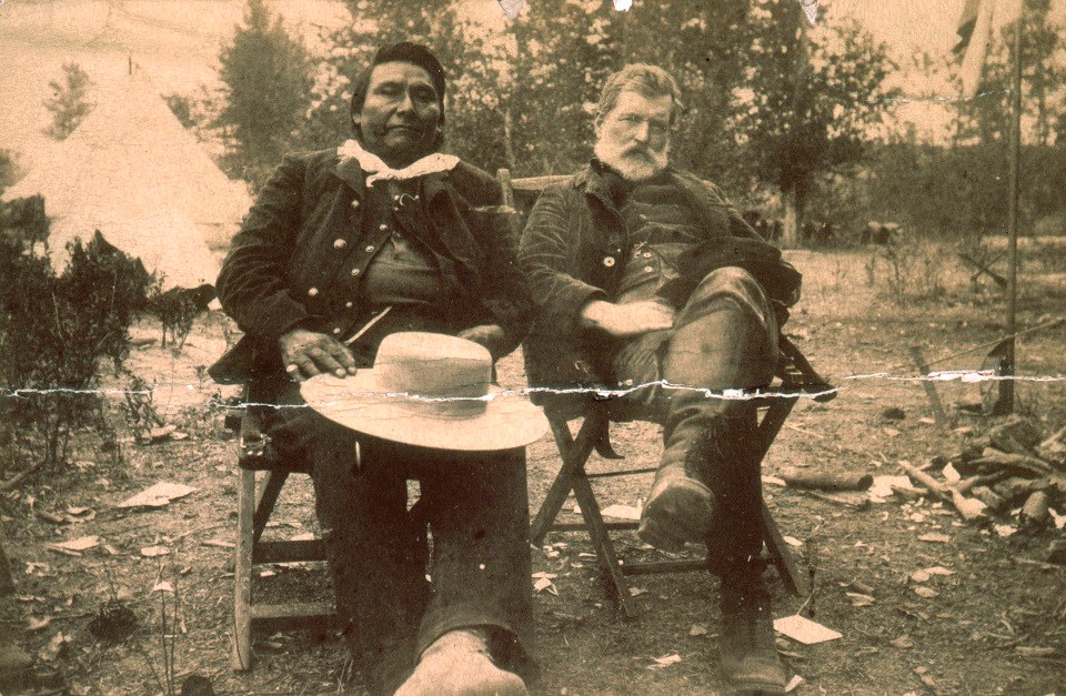 A black and white photo of Chief Joseph and John Gibbon sitting in chairs outdoors.