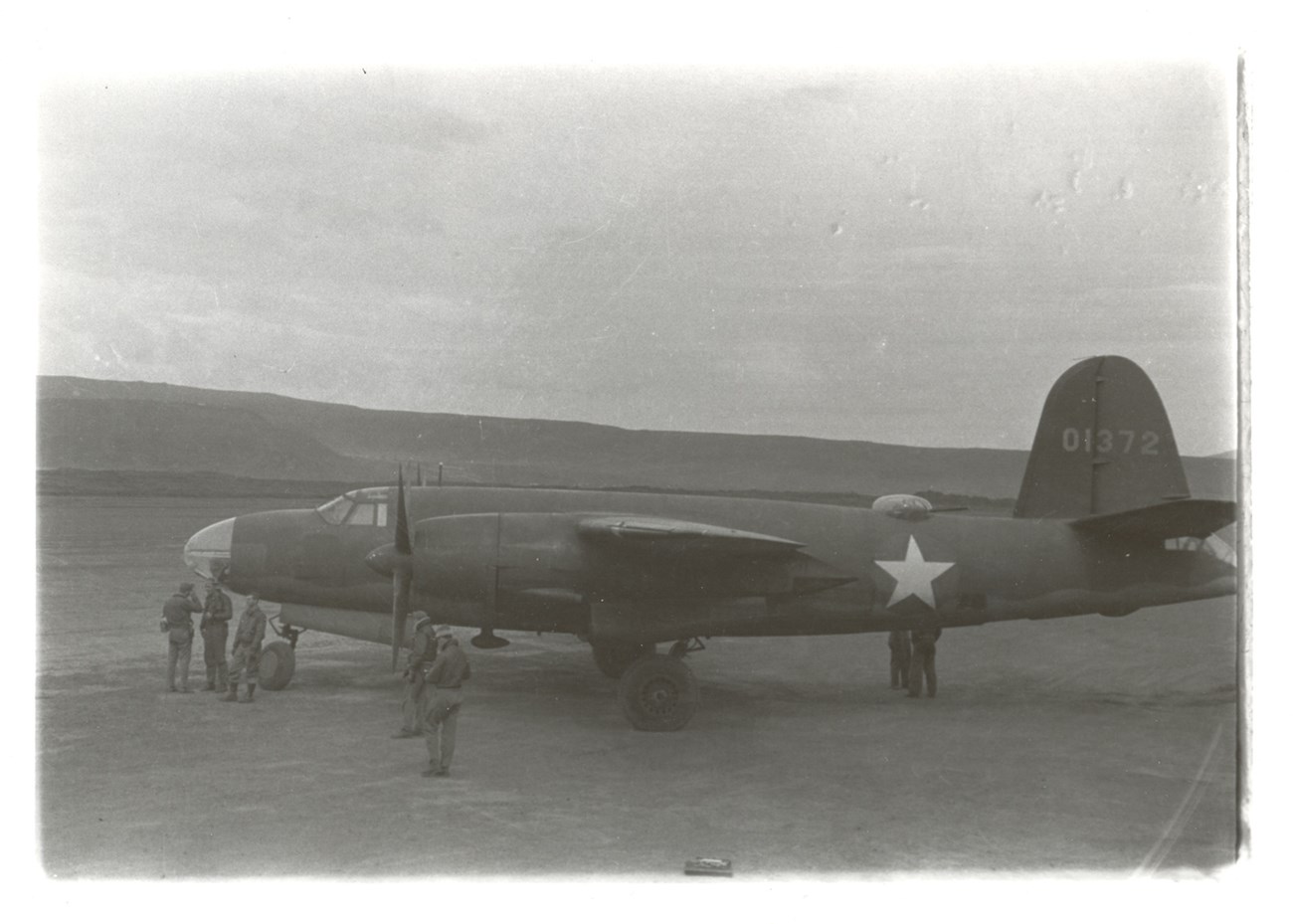 Side view of a plane with tail number, star on side, and people near the front propellers.