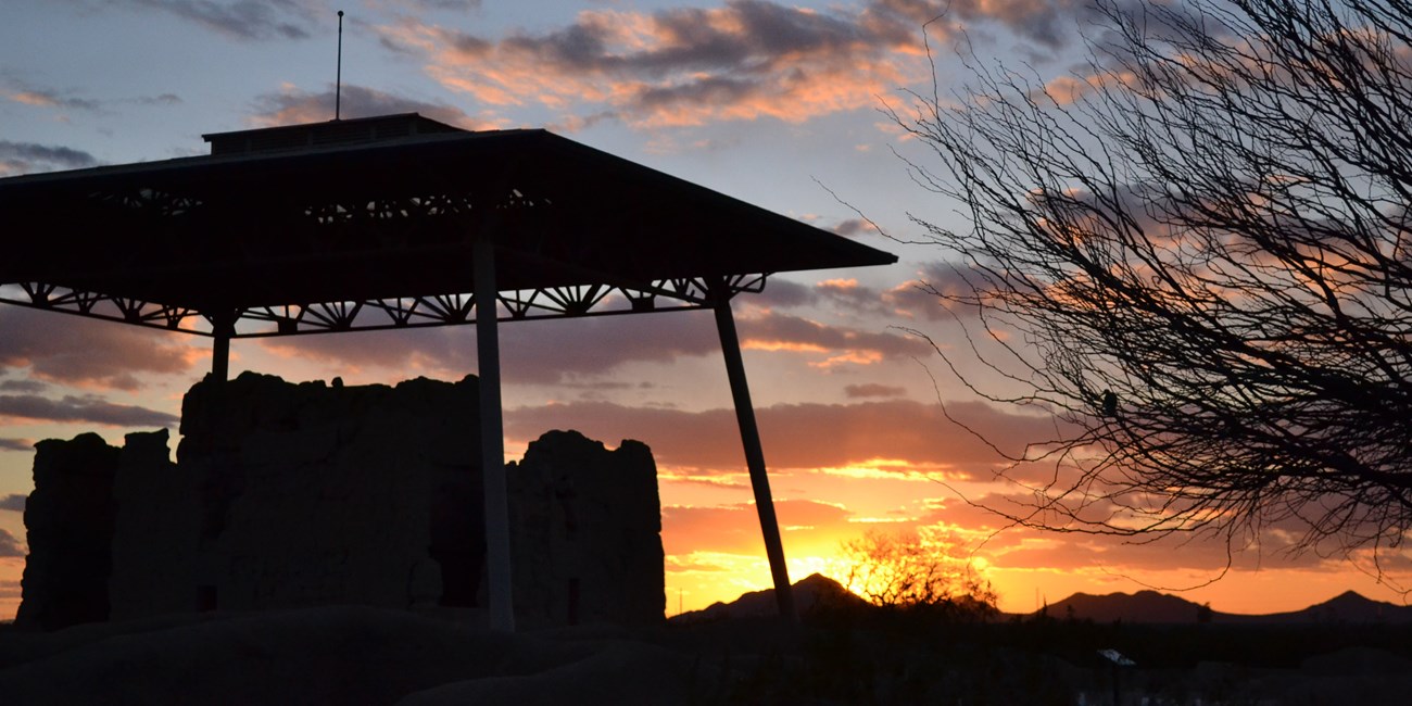The silhouette of the Casa Grande in front of a blue and orange sunset.