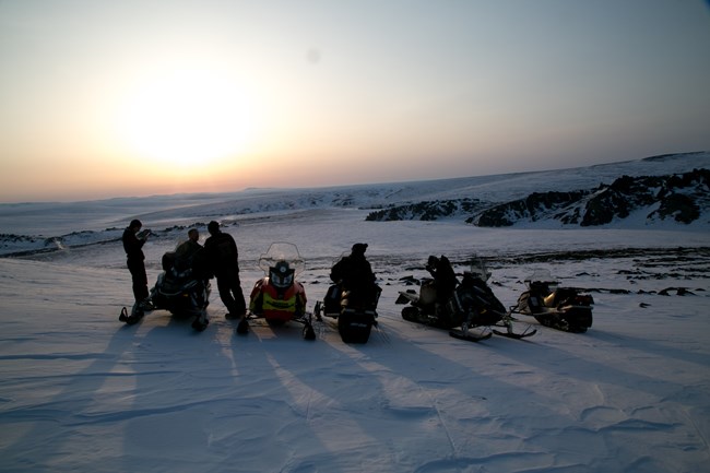 A group of people on snowmobiles on a small hill.