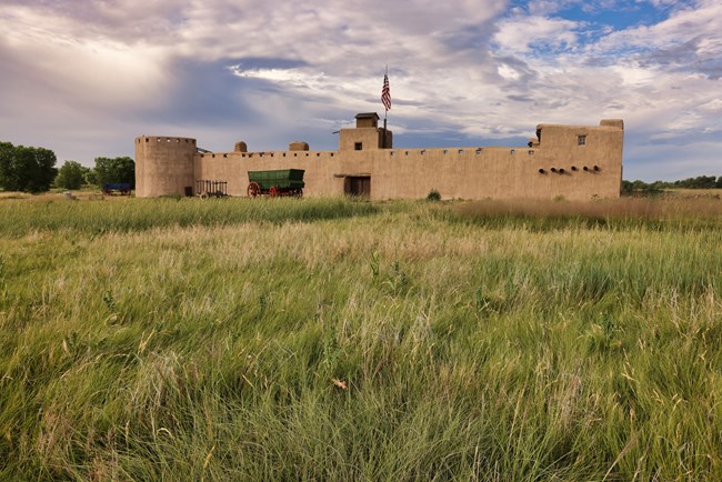 An old fort and a couple of old wagons under a cloud-filled sky.