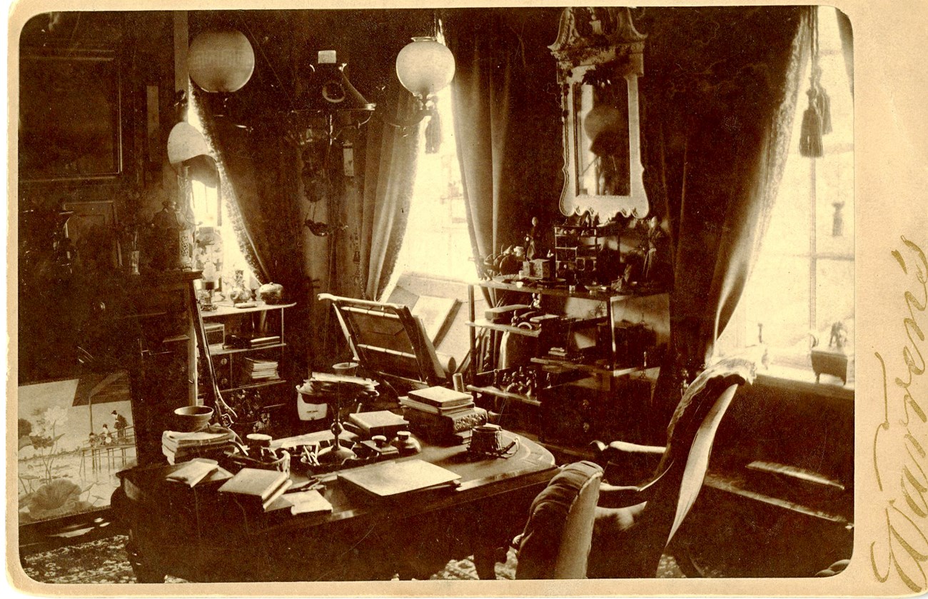 Sepia photograph of cluttered room with shelves and tables filled with small decorative objects