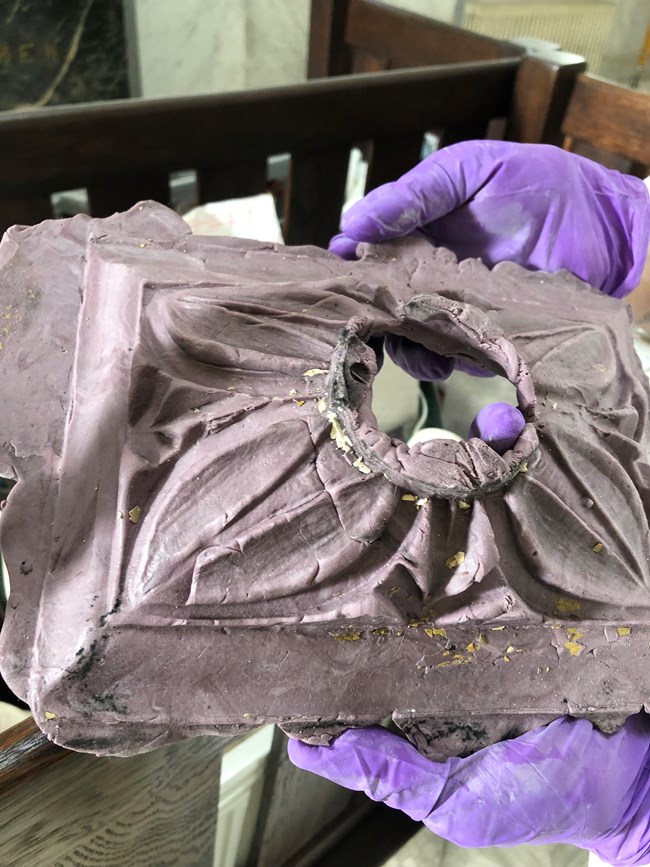 BHLodgeMedallionMold Someone with purple gloves holding a plaster mold of a floral medallion.