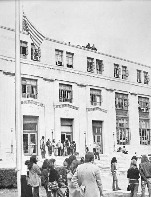 A crowd stands in front of building