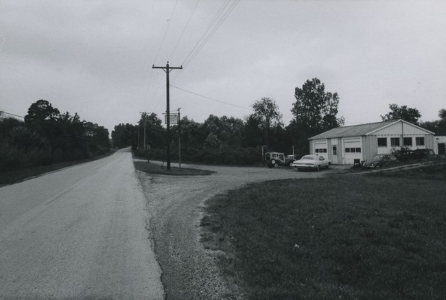 Tonkin Auto Shop A two-bay garage stands along a rural road, marked by a sign hanging on a high pole.