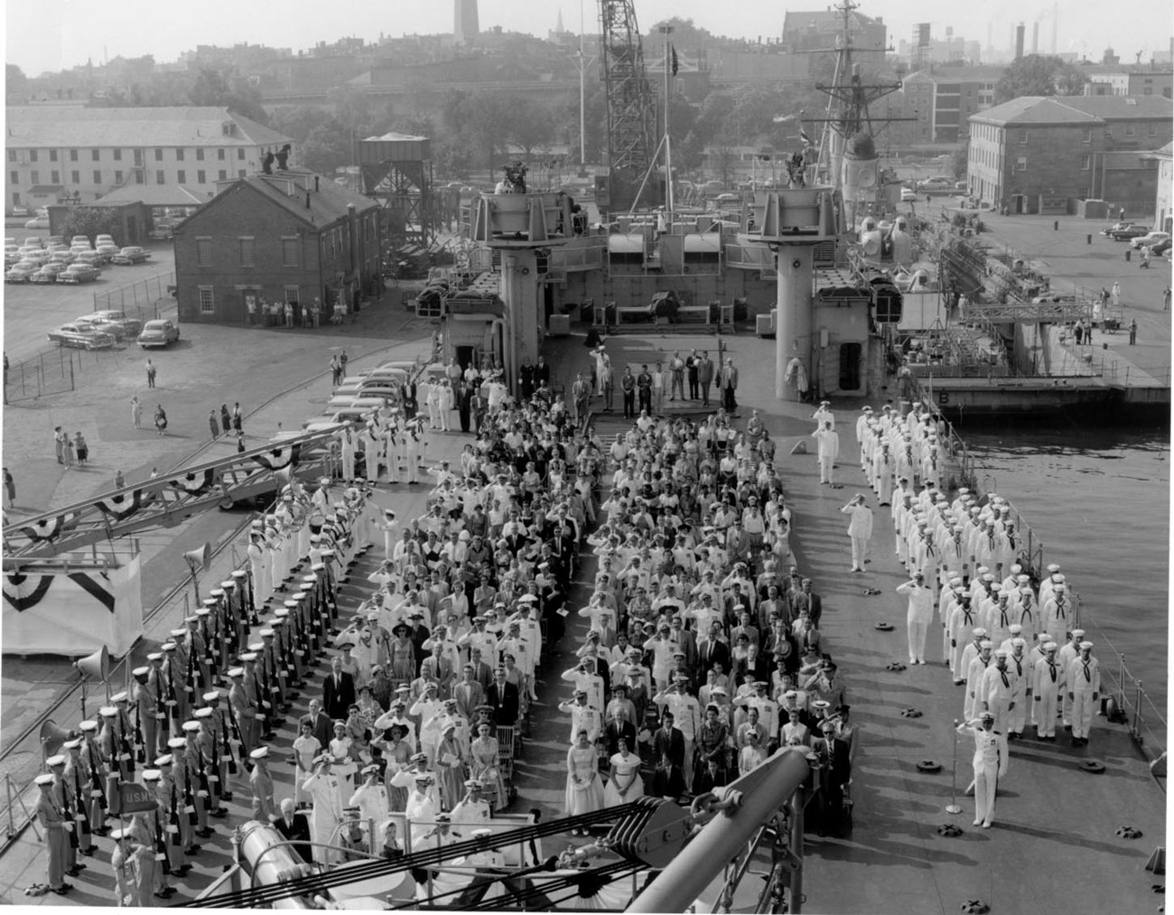 a ship's commissioning ceremony with sailors lined up and an audience of military personnel and civilians.