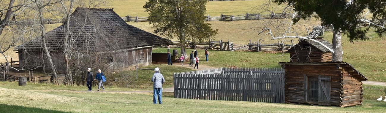 Park visitors walking around a cabin with a split-rail fence in the background.