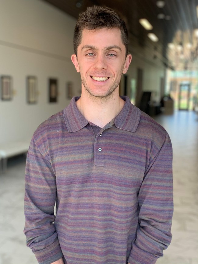 Dr. Ben Pokross White man with short brown hair and stubble wearing a purple shirt.