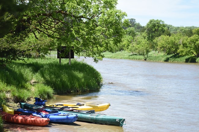 Kayaks resting on the shore of the river.