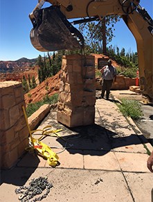 Backhoe Column Fence Shovel of backhoe suspended above rock columns and yellow straps at collapsed fence